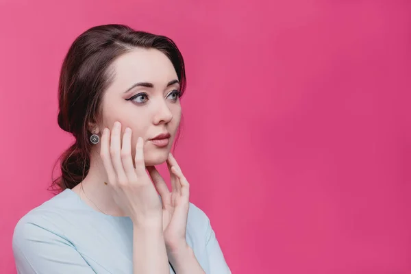 Menina bonita balança o rosto com as mãos em um fundo rosa no estúdio. O conceito de cuidados com a pele . — Fotografia de Stock
