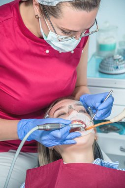 Bir dişçi hastayı muayene eder, hastaya yakından bakar. Ağzı açık bir şekilde dişçi eşyasının yanında durur. Tıp merkezlerinde sağlık ve tedavi kavramı