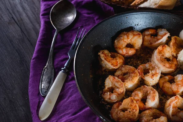 Los langostinos fritos en la cacerola sobre la mesa con el pan, la granja que sirve la comida, el fondo oscuro. El concepto de nutrición y hermosa porción de comida — Foto de Stock