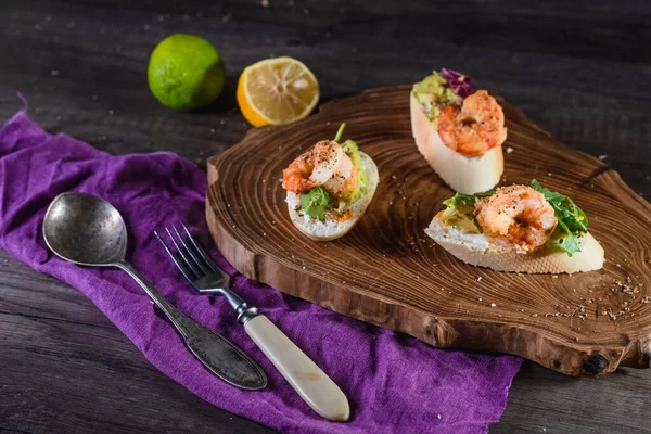 Sandwiches con camarones, queso y aguacate sobre una bandeja de madera sobre la mesa, fondo oscuro. El concepto de nutrición y hermosa porción de comida — Foto de Stock