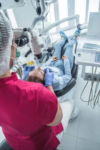 O médico dentista olha em um microscópio para os dentes do paciente. O conceito de cuidados de saúde e tratamento em instalações médicas — Fotografia de Stock