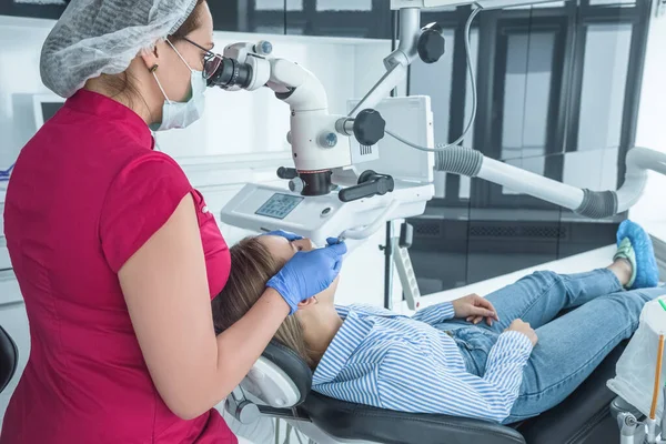 El médico dentista mira con un microscopio los dientes del paciente. El concepto de atención y tratamiento de la salud en las instalaciones médicas — Foto de Stock