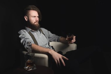 Elinde bir bardak alkolle izole edilmiş siyah bir arka planda dalgın genç bir adamın portresi. Eğlence, dinlenme ve rahatlama kavramı.