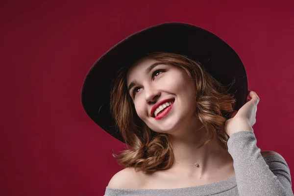 Retrato de uma menina bonita que endireita um chapéu em um fundo vermelho. O conceito de beleza e juventude — Fotografia de Stock