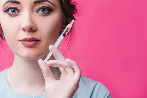 Mulher cosmetologista médico com uma seringa nas mãos em um fundo rosa no estúdio. O conceito de cosmetologia, medicina e beleza — Fotografia de Stock