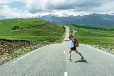 Sırt çantalı genç bir kız dağlarda bir yolda duruyor. Seyahat ve tatil otostop konsepti