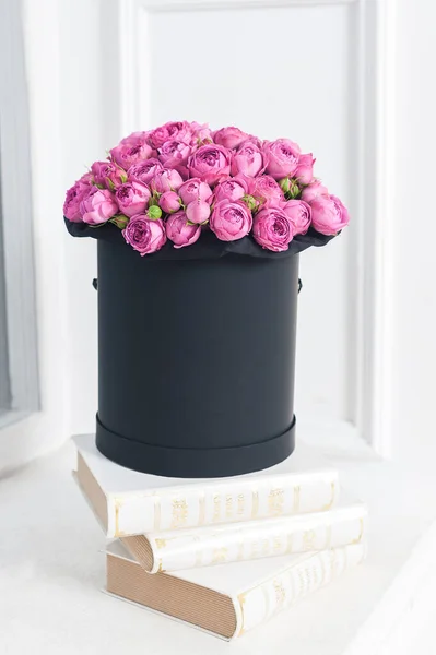 Yuvarlak siyah bir kutuda bir buket çiçek kitapların üzerinde duruyor. Pembe güller.