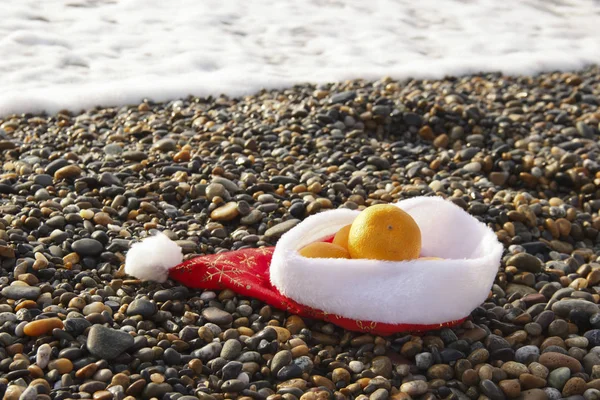 Sombrero de Santa Claus con mandarinas en la playa —  Fotos de Stock