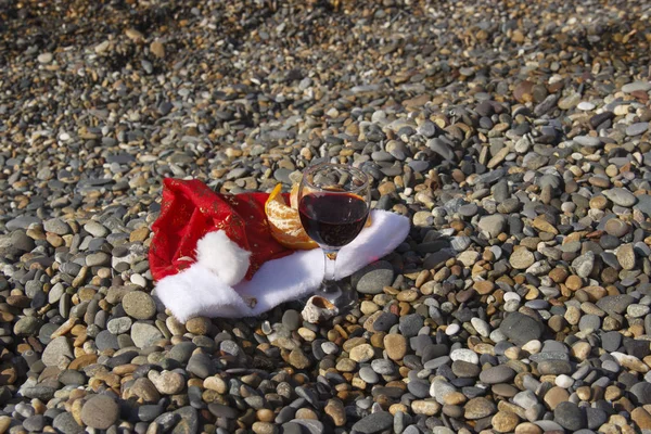 Egzotyczny Nowy Rok i Boże Narodzenie na morzu. Butelka i szklanki na plaży morskiej. napój winny, czapka Świętego Mikołaja nad morzem symbolizująca obchody Nowego Roku w upalny klimat lub pogodę. — Zdjęcie stockowe