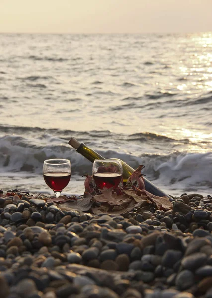 Ripe pomegranate fruit with a glass of wine and a bottle on the beach. Romantic day at the seaside.