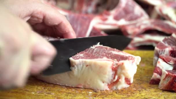 Avec un couteau tranchant sur une planche de bois couper la viande d'agneau gras — Video