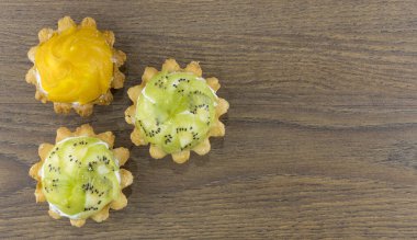 Tahta arka planda doldurulmuş sepet şeklinde kurabiyeler. Kremalı ve meyveli hamur işi. Sevgililer Günü için tatlı ikramları