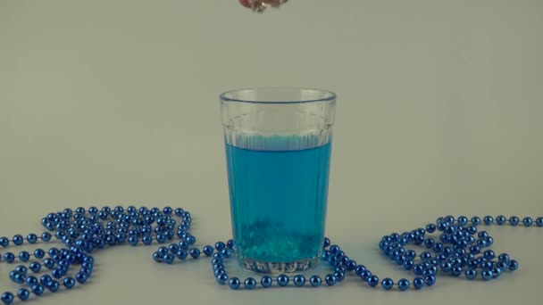 Líquido azul en un vaso con hielo sobre un fondo blanco — Vídeo de stock