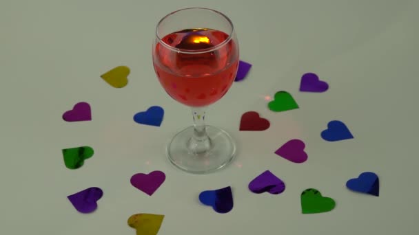 Sklenice červeného vína na bílém pozadí. roztroušené konfety ve tvaru srdcí. koncepce Valentýnské oslavy. — Stock video