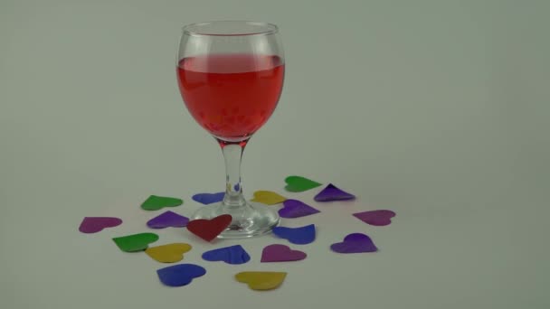 Copa de vino tinto sobre fondo blanco. una dispersión de confeti en forma de corazones. concepto de celebración del día de San Valentín . — Vídeo de stock