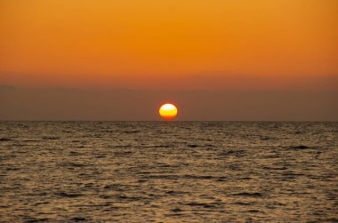 Denizde güneşli güzel bir gün batımı. Sahildeki muhteşem yaz manzarası. Karadeniz 'de alevli günbatımı manzarası ve üzerindeki turuncu gökyüzü. Sakin dalgalarda muhteşem güneş ışığı yansıması.