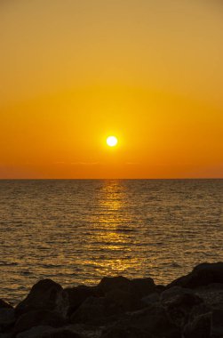 Denizde güneşli bir gün batımı. Sahildeki muhteşem yaz manzarası. Karadeniz 'de alevli günbatımı manzarası ve üzerindeki turuncu gökyüzü. Sakin dalgalarda muhteşem güneş ışığı yansıması..