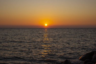 Denizde güneşli güzel bir gün batımı. Sahildeki muhteşem yaz manzarası. Karadeniz 'de alevli günbatımı manzarası ve üzerindeki turuncu gökyüzü. Sakin dalgalarda muhteşem güneş ışığı yansıması.