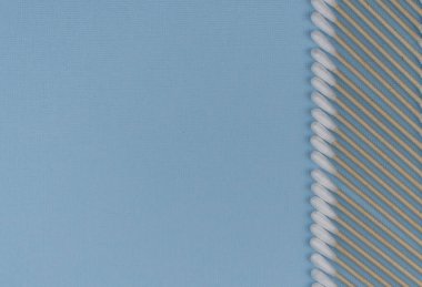 Mavi zemin üzerinde pamuk çubukları olan düz bir kompozisyon. Pamuk ve bastondan yapılmış doğal pamuk çubukları. Hijyen ve hijyen. Üst görünüm kulak çubukları.