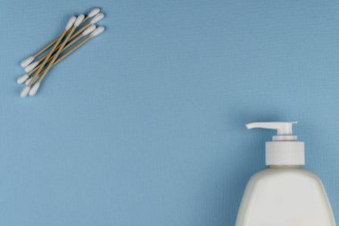 Mavi arka planda dezenfektan jeli ve doğal pamuk çubuklu düz kompozisyon. Hijyen ve hijyen. Üst manzara, kulak çubukları..