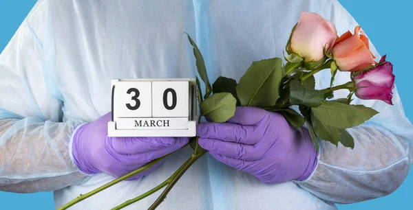 doctor with a bouquet of flowers in his hands. medical worker in surgical gown and medical gloves. Close- up of a bouquet of beautiful roses. National Doctor\'s Day March 30