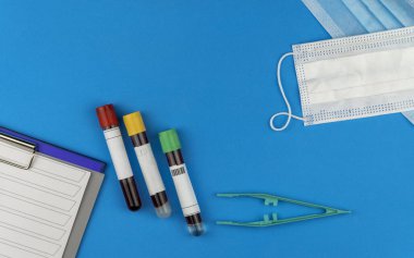Düz bileşim, mavi arka planda kan testi tüpü ve antiviral tıbbi maske vardı. Salgın ve karantina Coronavirüs COVID-19.