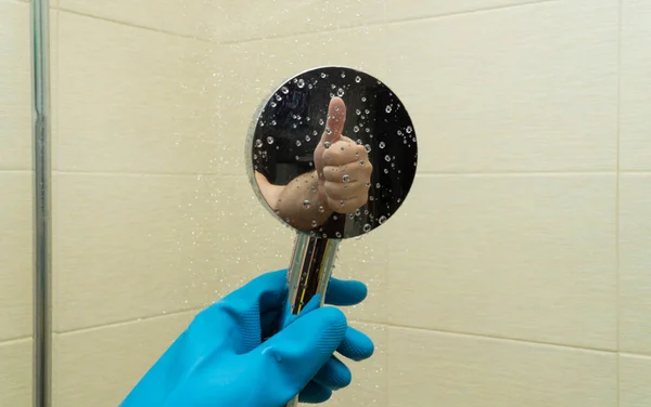 shower watering can in hands with rubber gloves. cleaning the bathroom and cleaning the shower cabin. reflection of a hand making a kind gesture. concept of good and high-quality work. copy space.