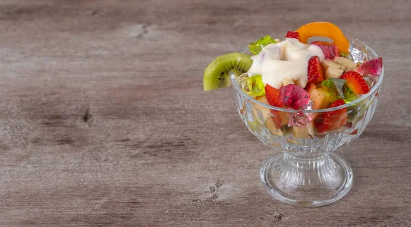 fresh fruit salad in a glass container on a wooden background. richest source of nutrients and vitamins. juicy and fresh berries, the concept of healthy and dietary food.