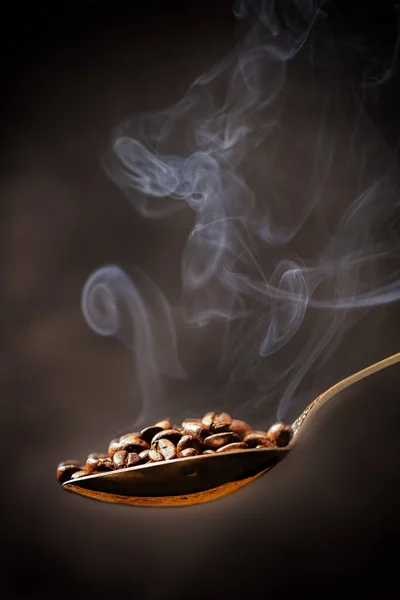 Gümüş kaşıkta kahve taneleri. Siyah bir arka planda. Sıcak tanelerden çıkan buhar görülebilir..
