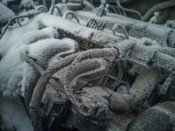 Arabanın motorunun bir kısmı yakın plan. Uzun bir park süresinden sonra motor bölmesi kar ve buzla kaplıdır..