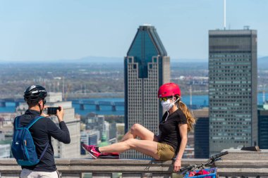 Montreal, CA - 18 Mayıs 2020: Coronavirus salgını sırasında maske takan genç bir kadın Montreal ufuk çizgisi önünde poz veriyor.