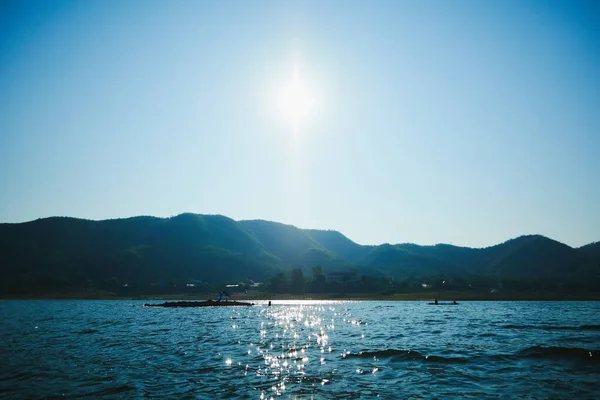 A bright sun in the sky with a lake and mountain background.