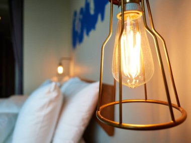 Bir odada başucu tungsten lambası. Ampulün çelik bir çerçevesi var..