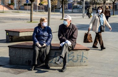 Bosna-Hersek 10 Nisan 2020: Solunum maskeli insanlar bankta oturuyor, korona virüsü salgını