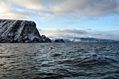 Norveç 'in Nordkapp belediyesi. Ülke, Avrupa 'nın en kuzey noktası olarak bilinen 307 metre yüksekliğindeki kayalıklardan oluşuyor. Avrupa 'nın en kuzeydeki noktası Cape Nordkinn' dir. Yelkenli tekneden karlı tepelere bak.