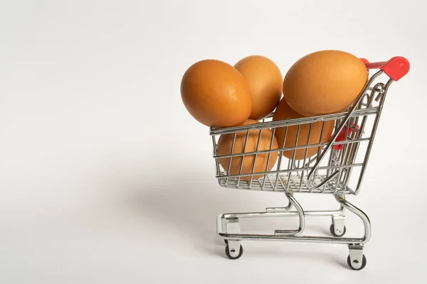 Toy little consumer food trolley from steel with red plastic handle on a gray background with five fresh egg inside. empty space