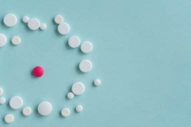 Mavi arka planda çeşitli şekillerde beyaz haplarla çevrili pembe bir hap. Tıbbi konsept. Çok renkli tabletler var. İlaç çemberi eczaneler için antiviral konsept, salgın ve hastalık içeriği.