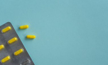 Tıbbi konsept. Paketlenmiş haplar, sarı kapsüllerde ilaç hapları. Mavi arka planda kabarcıklar. Eczane temalı. ilaç, reçete, hastalık. Boşluğu kopyala.