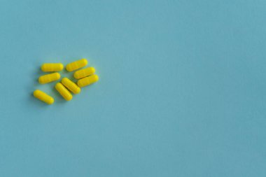 Mavi arka planda kapsül şeklinde sekiz sarı tablet. Tıbbi konsept. İlaç hapları, eczane teması. ilaç, reçete, hastalık. Boşluğu kopyala.