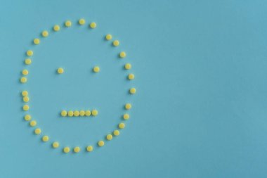 Tarafsız duygusal yüz, mavi arka planda küçük sarı tabletlerden alınmış emoji. Adım adım. İkinci adım: üzüntü. Tıbbi konsept, hastalık, ilaç, iyileşme. Boşluğu kopyala