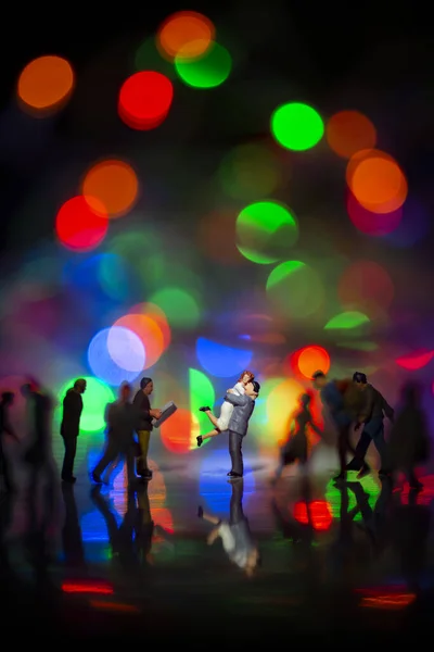 Miniature toy -A couple hugging together among busy commuters crowd with colorful bokeh lights, happiness concept.