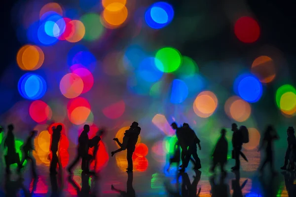 Miniature toy - Silhouette of a couple hugging together among busy commuters crowd with colorful bokeh lights, happiness concept.