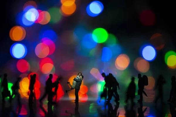 Miniature toy -A couple hugging together among busy commuters crowd with colorful bokeh lights, happiness concept.