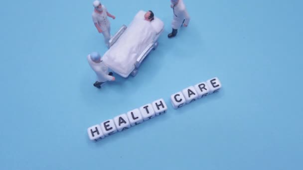 ミニチュア医療用おもちゃの人々 青やティールの背景を持つ健康管理文 パンアップ — ストック動画