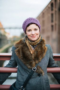 Gülümseyen Kafkas kadın portresi. Başında ve omuzlarında kalın giysiler ile kameraya bakıyor. Örgü bir şapka takıyor ve Georgetown, Washington DC 'de bir kanalın üzerinde duruyor.. 