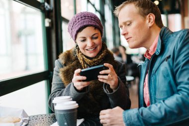 Kafeteryada oturup kahve içen ve el yapımı akıllı telefon kullanan çekici beyaz bir çift. 