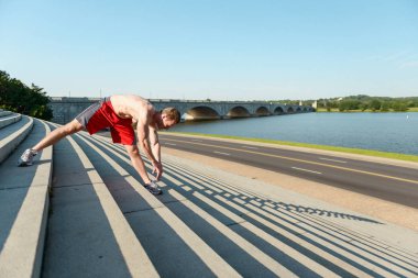 Fit caucasian man stretching on steps during an intense outdoor workout in the early morning in Washington DC