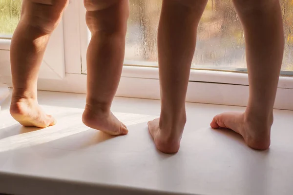 Children\'s bare feet. Sisters with flat feet on a white background, looking out the window, indoors