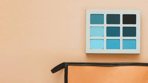 Bolso de maquillaje naranja rosa y paleta de sombras azul turquesa sobre fondo melocotón — Foto de Stock