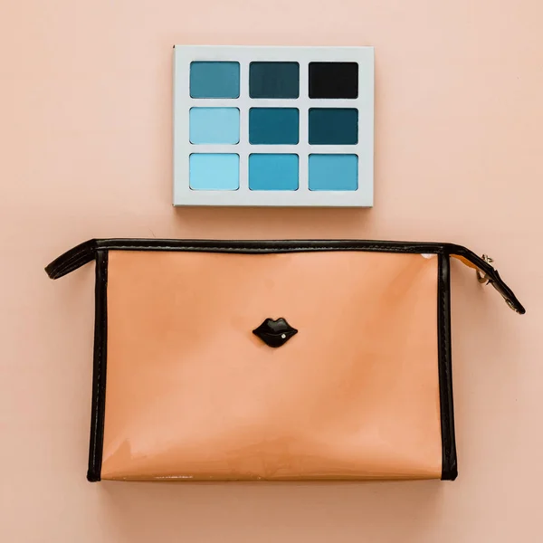 orange pink makeup bag and turquoise blue eye shadow palette on a peach background